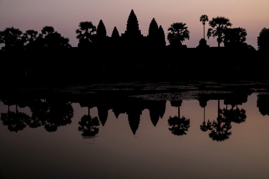 Angkor Wat silhouetted against a pink dawn sky and reflected in the moat